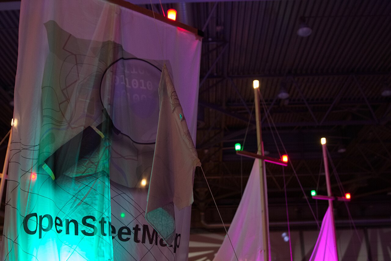 Powiewający sztandar prezentujący logotyp OpenStreetMap na białym tle.