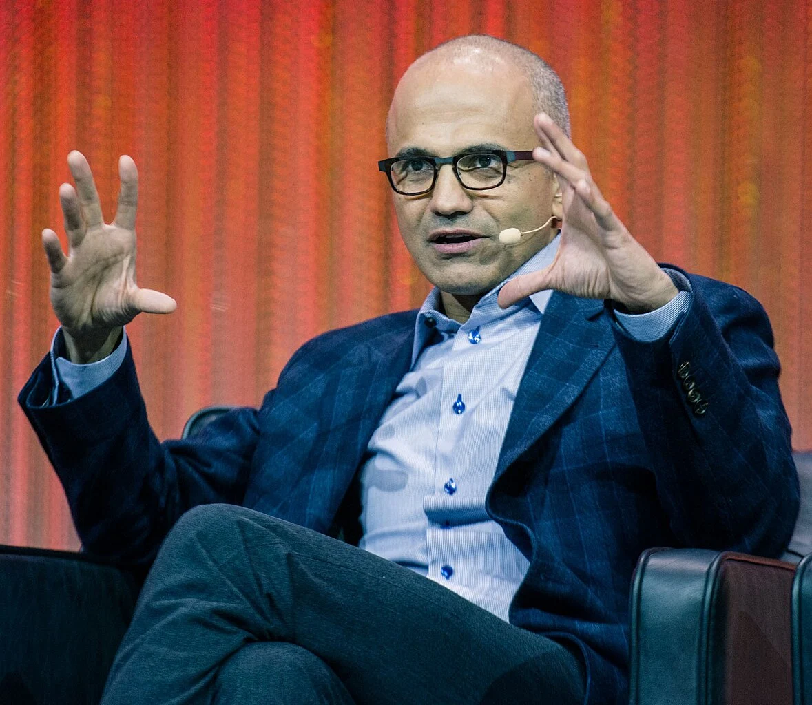 Satya Nadella, prezes Microsoftu, rozkłada ręce, przemawiając przez mikroport.